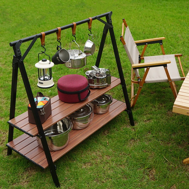 Outdoor setup with a metal stand, pots, pans, and camping gear on a grassy field.