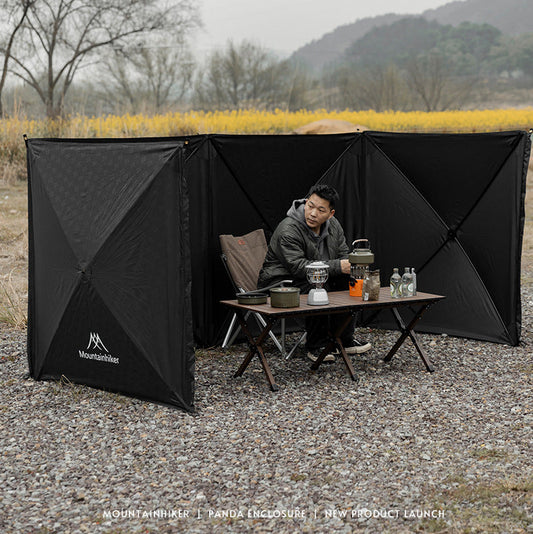 Person sitting at a table with a black outdoor privacy screen in a natural setting